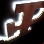 Groot, verlicht logo met een gebogen letter en een metallic afwerking op een donkere achtergrond.