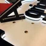 Verlichte, zwarte letters liggen op een witte achtergrond, met enkele zichtbare goudkleurige bevestigingsschroeven.