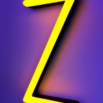 Gele neonletter "Z" met een zwarte rand, geplaatst tegen een paarse achtergrond.