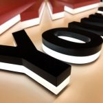 Zwarte, driedimensionale letters met een witte verlichting aan de onderkant, geplaatst op een lichte achtergrond.